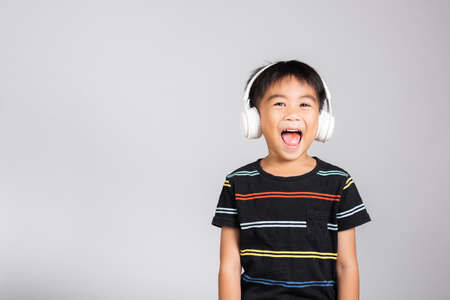 Little cute kid boy 5-6 years old listen music in wireless headphones in studio shot isolated on white background, happy Asian children smiling listening audio, entertainment lifestyleの写真素材
