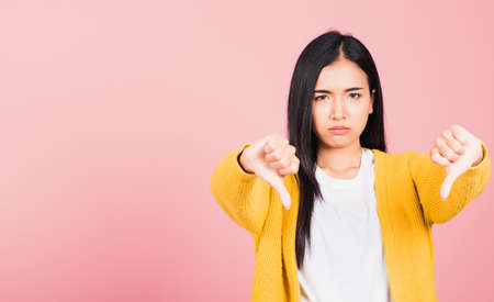 Portrait Asian beautiful young woman unhappy, negative gesture showing finger thumbs down or dislike...