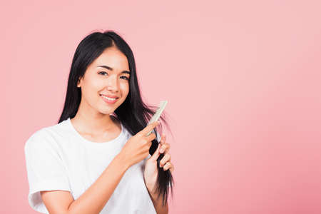 Portrait of Asian beautiful young woman smile combing her hair, happy female long healthy hair with hairbrush brushing hairs, studio shot isolated on pink backgroundの写真素材