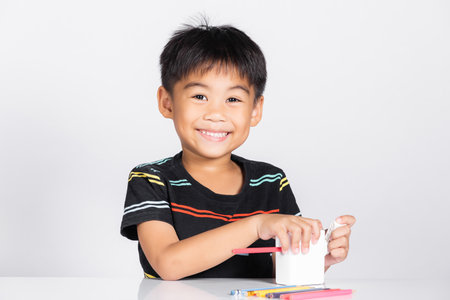 Little cute kid boy 5-6 years old smile using pencil sharpener while doing homework in studio shot isolated on white background, Asian children preschool sharpening color pencils, education conceptの写真素材