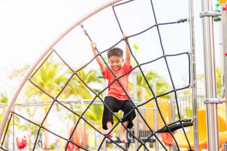 Asian child smiling playing climbing outdoor playground, happy preschool little kid having funny while playing climbs on a rope climbing net on playground equipment in daytime in summer, Little boyの写真素材