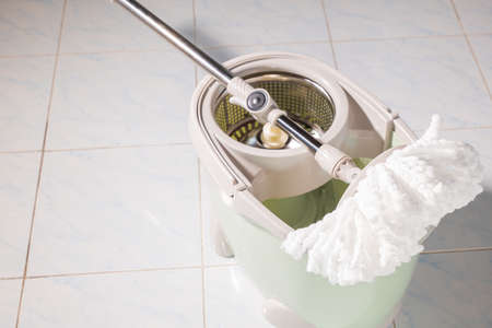 Mop with microfiber head spinning on the bucket next to floor cleaning liquid and mopping the floor...