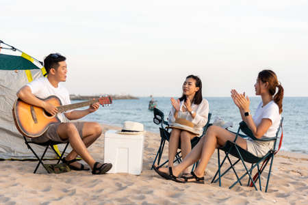 Happy friend have fun playing guitar and clap in camp they smiling together in holiday on sand beach...