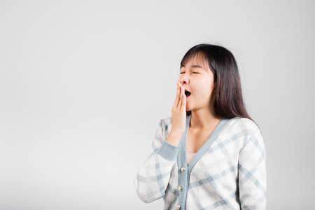 Sleepy woman closed eyes emotions tired and sleepy her yawning cover mouth open by hand, Portrait Asian beautiful young female sleep and energy studio shot isolated on white background with copy spaceの写真素材