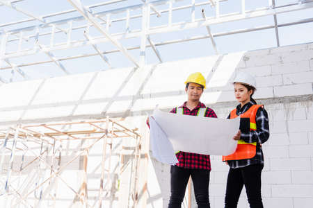 Architect and client discussing the plan with blueprint of the building at construction site. Asian...