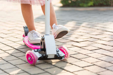 Child riding scooter. Happy Asian little kid girl wear safe helmet playing pink kick board on road in park outdoors on summer day, Active children games outside, Kids sport healthy lifestyle conceptの写真素材