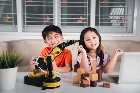 Two children programming and testing robot arm their science, Kid little girl program code to robot with laptop computer and the boy test with remote control to pick up wood block, education lessonの写真素材
