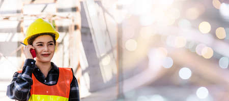 Asian engineer foreman architect worker woman working at building construction site talking with radio, engineering hold radio discuss operate and control worker employee to building constructionの写真素材