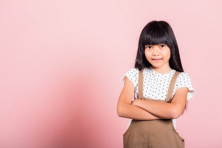Asian little kid 10 years old smiling with arms crossed at studio shot isolated on pink background,...