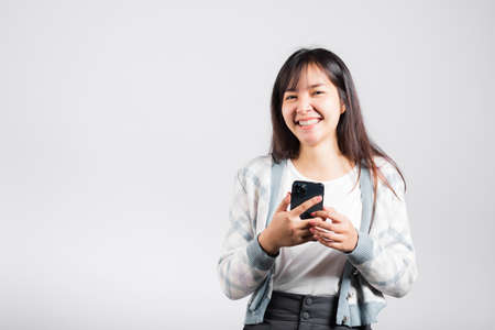 Woman excited read social network feedback on smartphone studio shot isolated white background, young female smiling typing sms message on mobile phone in social mediaの写真素材