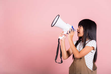 Asian little kid 10 years old shouting by megaphone at studio shot isolated on pink background, Happy child girl lifestyle she screeching through in megaphone announces discountsの写真素材