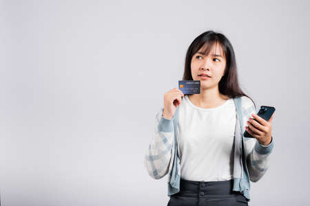 Woman excited smiling hold mobile phone and plastic debit credit bank card for payment studio shot...