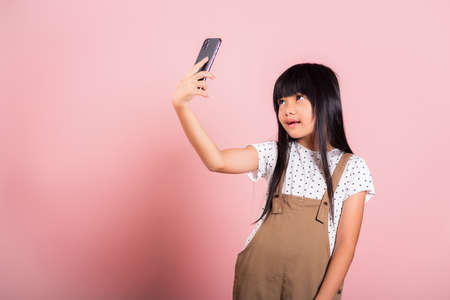 Asian kid 10 years enjoying using mobile phone take selfie at studio shot isolated on pink background, Happy child girl lifestyle using smartphone making video selfieの写真素材