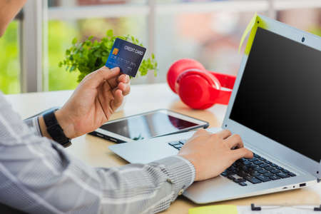 Asian business man hand holding credit card and typing entering security code on a laptop computer for process payment online shopping on the internet at the home officeの写真素材