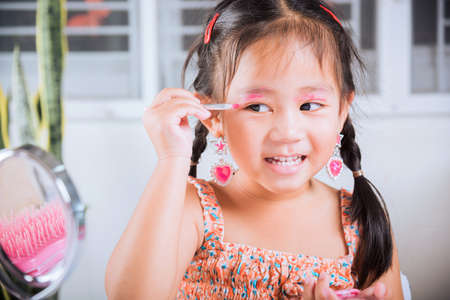 Happy kid is beautiful make up with cosmetics toy, Asian adorable funny little girl making makeup her face she applying carborundum eyeliner to eyelid, Learning activity to be woman at houseの写真素材