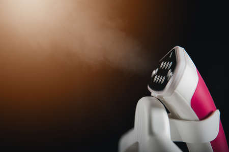 Close up of electric hand steam generator while it's hot and steam comes out on the ironing board place for clothes on black background, Household & home equipment for housework, concept of linen careの写真素材