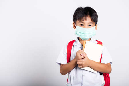 Asian student kid boy wearing student thai uniform and medical protect face mask and hugging note book in studio shot isolated on white background, new normal back to schoolの写真素材