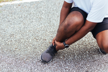 Close up Asian young sport runner black man wear watch hands joint hold leg pain because of twisted ankle broken while running at the outdoor street health park, healthy exercise Injury from workoutの写真素材