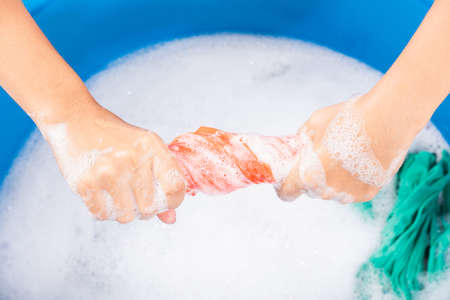 Closeup young Asian woman use hands washing color clothes in basin. Female squeeze wring out wet fabric cloth with detergent have soapy bubble in water, studio shot background, laundry conceptの写真素材