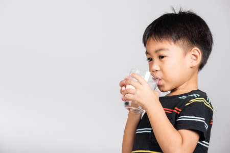 Little cute kid boy 5-6 years old smile drinking fresh water from glass in studio shot isolated on white background, Asian children preschool, Daily life healthの写真素材