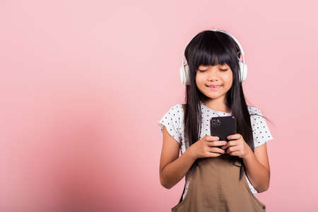 Asian kid 10 years enjoying listening music from mobile phone wear wireless headset closed eyes at...
