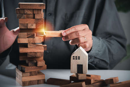 Alternative risk plan. Business hand playing tower wooden blocks game, man pull one wood block from...