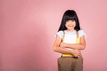 Asian little kid 10 years old holding book for going to school at studio shot isolated on pink...