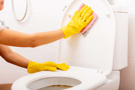 Hands of Asian woman cleaning toilet seat by pink cloth wipe restroom at house, female wearing yellow rubber gloves she sitting and cleanup or washing bathroom, Housekeeper healthcare conceptの写真素材