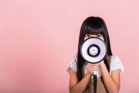 Asian little kid 10 years old shouting by megaphone at studio shot isolated on pink background, Happy child girl lifestyle she screeching through in megaphone announces discountsの写真素材
