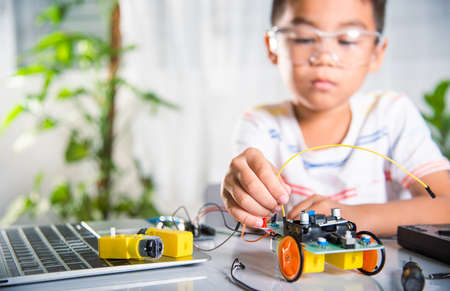 Little child remotely learn online with car toy before sent code, Asian kid boy plugging energy and signal cable to sensor chip with Arduino robot car, STEAM education AI technology course learningの写真素材