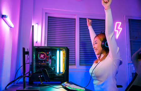 Winning Victory. Asian gamer playing online video game excited on desktop computer PC colorful neon LED lights, young woman in gaming headphones using computer she happy successful, E-Sport conceptの写真素材
