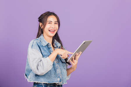 Portrait of Asian beautiful young woman smiling using tablet computer, Happy lifestyle female teen touching screen on digital tablet pc, studio shot isolated on purple backgroundの写真素材