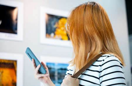 Visitor woman standing takes picture art gallery collection in front framed paintings pictures on...
