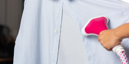 Close up of woman using electric hand steam generator while it is hot and steam comes out for clothes shirt at house, Household & home equipment for housework, concept of linen careの写真素材