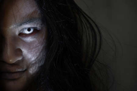 Scary ghost woman. Close up face of Asian woman ghost or zombie horror creepy scary have hair covering the face her eye at abandoned house dark tone, female make up zombie face, Happy Halloween dayの写真素材
