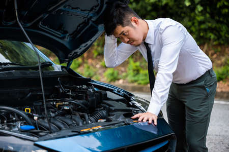 Asian businessman car broken breakdown, young stressed man having trouble car failure problem looking in frustration at failed engine in the morning, accident on road outdoor, late for workの写真素材