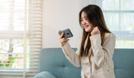 Excited woman use mobile phone raising fist up she celebrating victory win online or received good...
