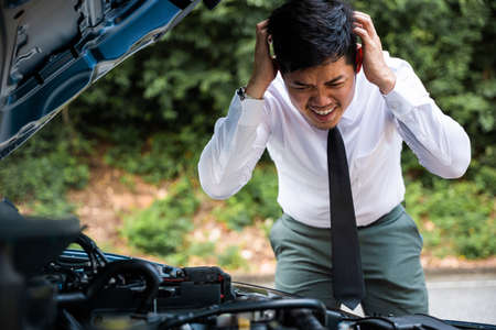 Asian businessman car broken breakdown, young stressed man having trouble car failure problem looking in frustration at failed engine in the morning, accident on road outdoor, late for workの写真素材