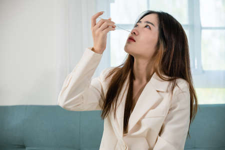 Asian woman using rapid antigen test kit for selftest nose swab test for possible infection, female holding perform fast  ATK self test at home in living room, Introducing device nasalの写真素材