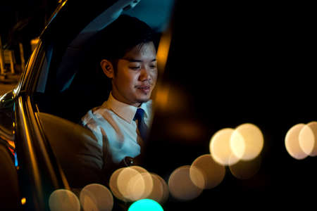 Businessman using smartphone in backseat of car near window at night, Handsome Asian young man work...