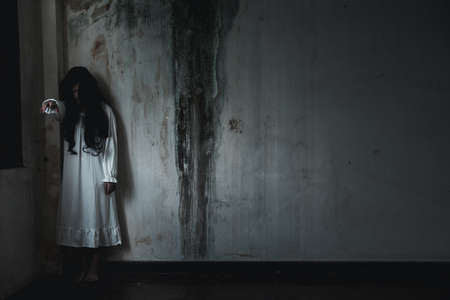 Scary ghost woman. Asian ghost or zombie horror creepy scary have hair covering face and eye reach arm out at abandoned house dark room, female makeup terror zombie face, Happy Halloween day conceptの写真素材