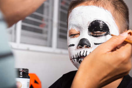 Portrait of woman applying color brush to child face for party at home, family Asian mother and kid son getting makeup halloween face painting look like ghost, Happy halloween day conceptの写真素材
