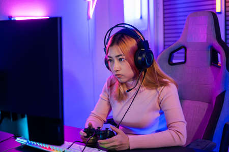 You win. Gamer using joystick controller plays online video game with computer neon lights she winning, woman wear gaming headphones playing live stream esports games console at home celebrating winの写真素材