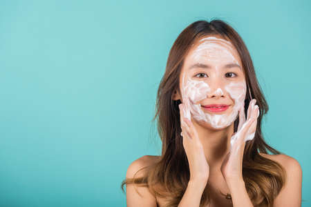 Asian woman face wash exfoliate scrub soap foam with skincare cleansing, Portrait beautiful female smile applies foaming cleanser healthy skin, Studio isolated on blue background, beauty skincareの写真素材