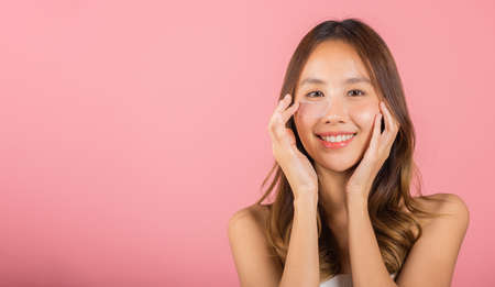 Anti aging. Asian beautiful young woman smiling mask cosmetic patches gel under the eyes, Portrait female applying medical hydrogel eye patch on face, studio shot isolated on pink background, skincareの写真素材