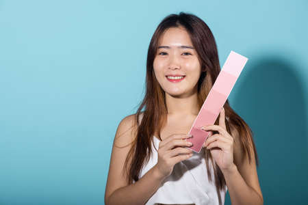 Portrait of happy female hold color card under sun protection, skin beauty face, Asian beautiful young woman smiling and holding skin color scale paper studio shot isolated on blue backgroundの写真素材