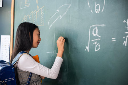 Education. Back view of school girl on science lesson in classroom write an answer on blackboard, primary child is standing in front of class in school writing chalkboard, Back to school conceptの写真素材