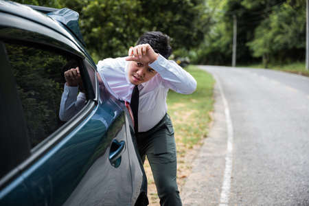 Asian businessman car broken has problems with car down during go to work in morning he pushing out...