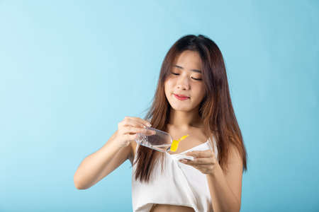 Facial Beauty Treatment Hygiene Skin. Happy Asian beautiful young woman drop removing cosmetic make up water to pad cotton face cleaner disc for cleaning, studio shot isolated on blue backgroundの写真素材