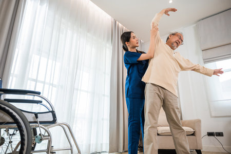 Rehabilitation of disabled people. Old senior man enjoys training with physiotherapist for outstretched arms at home, Asian physical therapist patient help elderly exercising arm stretchの写真素材